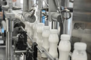 Gli scarti dell'industria lattiero casearia sono fra i più impattanti al livello di sostenibilità ambientale. Nella foto vediamo delle bottiglie di latte riempite dal macchinario di un'industria lattiero casearia.