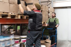 Fare outsourcing del magazzino è una delle soluzioni a cui le aziende ricorrono di più oggigiorno. Nella foto, due magazzinieri si occupano dello stoccaggio merci su alcune scaffalature.